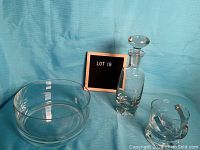 Full view of three glass items: one decanter with stopper, one clear round bowl, one clear ice bucket with metal handle, all on blue background.