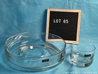 Photo showing a large clear glass chip bowl and a smaller dip bowl placed on a blue surface with a sign reading Lot 65 in the background.