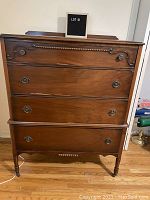 Full front view of vintage four drawer high boy dresser showing carved details and metal drawer pulls, wood finish, and overall condition.