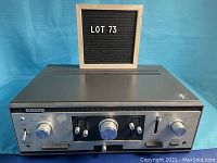 Front view of vintage Sony TA-1144 integrated stereo amplifier placed on blue surface with a wooden frame behind showing lot number.