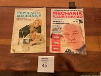 Top view of two magazines laid flat on wooden surface: Popular Mechanics 1966 February issue and Mechanix Illustrated 1971 February issue