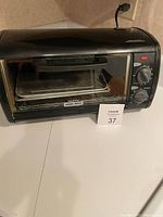 Front view of Black & Decker toaster oven showing control dials, handle, and interior tray.