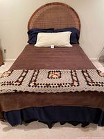 Photo showing full size bed with dark wood frame and rounded wicker headboard, brown and navy bedding, and crocheted blanket.