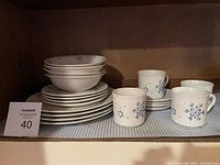 Photo of stacked cereal bowls, dinner plates, salad plates, and coffee mugs with saucers in shelf.