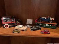 Full lot shot showing all toy cars on wooden shelf including Hershey's truck, Roadster in front, and four smaller cars.