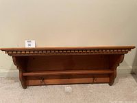 Image of wooden wall shelf showing carved trim and hooks underneath.