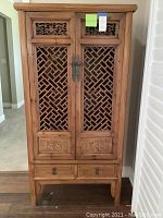 Front view of wooden armoire showing carved lattice doors, metal handles, and two drawers at bottom.