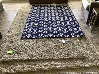 Photo showing two beige shag rugs stacked with blue and white rug on top, on tile floor.