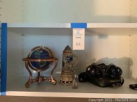 Shelf with globe on a bronze metal stand, miniature German stein music box, pewter tennis figurine, and Sears binoculars in case