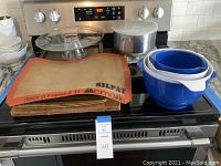 Photo showing the silicone baking mat with Silpat branding, three nesting mixing bowls in blue and white, and wooden cutting board underneath on stovetop