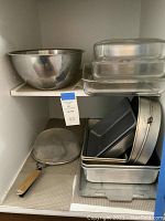 Three glass baking dishes in graduated sizes stacked next to a large stainless steel bowl on the shelf, with a mesh sifter on the side.