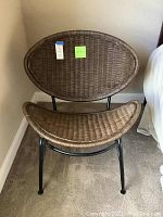 Front view of the wicker chair showing the curved wicker seat and oval backrest with metal frame.