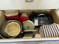 Drawer view showing plastic storage containers, metal steamer insert, metal skimmer, plastic colander, kitchen towels and other kitchen items.