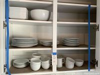 Cupboard with stacked white rectangular and round dishes, mugs and bowls.