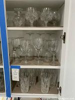 Shelf with various crystal and glass stemware including tumblers and wine glasses.