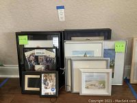 Photo showing a group of assorted framed art pieces in varying sizes including paintings, prints, and collageing along with a digital photo frame in black frame.