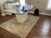Dining table with beveled glass top resting on stone base shown with rug underneath on hardwood floor.