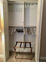 Closet with wood, plastic, and felt hangers on hanging rods and wooden luggage rack on floor.