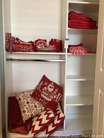 Closet shelving containing folded red and white holiday linens including pillows with Santa and snowflake patterns, blankets and tablecloths.