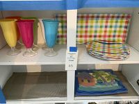 Photo showing six colored glasses and four square plaid plates with rectangular matching tray behind