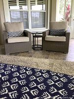 Two wicker chairs with cushions and pillows flanking nested side tables on porch