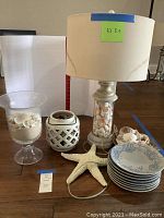 Full display of shell themed home decor showing lamp, shell containers, plates, and starfish on wood floor