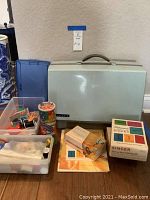 Overview of the lot showing the vintage Singer sewing machine hard case, sewing supplies in clear plastic containers, and Singer buttonholder kit box.