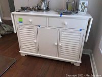 Three-quarter front view of buffet showing two drawers, three doors, drop leaves folded and items on top