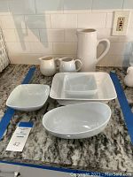Photo of all white ceramic serving pieces including pitchers and serving dishes arranged on countertop.