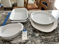 Photo of stacked white rectangular baking dishes and oval serving trays on a granite countertop.