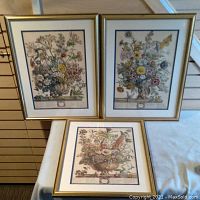 Three framed floral prints representing October, November, and December seasons arranged on surface and leaning against vertical surface.
