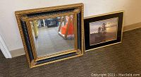 Photo of the gold and black ornate framed square mirror next to the framed nature print, showing both items and their size difference