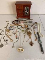 Full view of the wooden jewelry box with stained glass door, and the laid out jewelry assortment showing chains, lockets, pins, bracelets and watch.