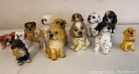 Photo showing all 14 dog figurines arranged in rows. Various breeds and colors represented, some holding 'Welcome' signs.
