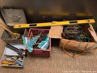 Wide shot showing assortment of tools in bins and boxes including hand tools and extension cords with a yellow Johnson level resting on top.