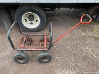 View of metal utility tool wagon showing red wire bed and handle, four wheels, and black frame.