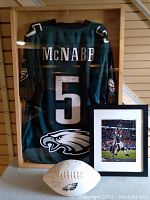 Overall view of wood and glass display case containing green McNabb jersey, framed photo and white panel football