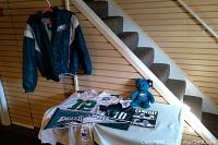 Full group of Eagles collectibles including jackets, jerseys, pennant, plush teddy, and program on table under stairs