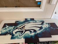 Full view of the 5-piece Philadelphia Eagles logo canvas wall art laid flat on a table, showing the entire logo and background design with lightning effects.