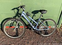 Side view of blue Realm Cycles women's mountain bike against a green wall showing full frame, tires and seat.