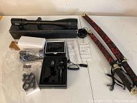 Wide view of two rifle scopes, mounts, instruction manuals, and two decorative katana swords with ornate scabbards and gold hilts.