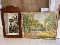 Photo showing both the wooden mirror with decorative carved top and the framed signed nature print by Robert Doares, set on the floor together.