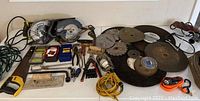 Overview of assorted tools showing saw blades, two circular saws, hand saw, clamps, drill bits, laser level, and extension cord.