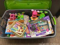 Top view of the large gray and green Sterilite bin filled with toys, including plastic houses, chalk, and boxed games.