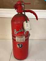 Full front view of the red vintage Randolph fire extinguisher showing label, handle and chain with tag.