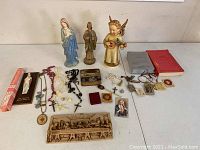 Overview photo of all religious items laid out on table including statues, rosaries, bible, plaques and small religious collectibles.