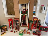 Large 3 ft tall wooden nutcracker in white foam and cardboard box surrounded by smaller boxed nutcrackers and other decorations on table