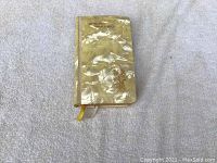 Prayer book with mother of pearl cover showing gold embossed text and cross emblem, closed, on light fabric background.