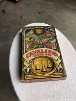 Top view of the Cavalier Chess Set box with vibrant artwork showing two players at a chessboard, some wear and dent on the box.