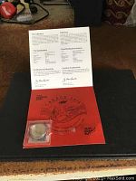 Photo of the coin in sealed plastic case with certificate of authenticity display card opened behind it
